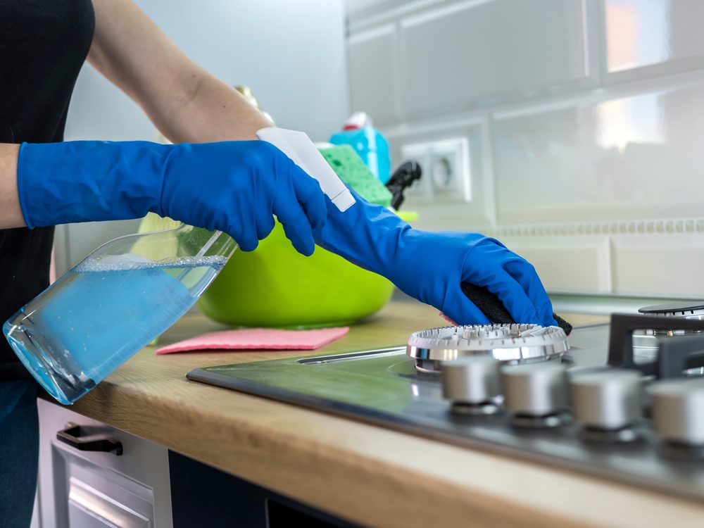 Gloved hands deep-cleaning a kitchen cooktop